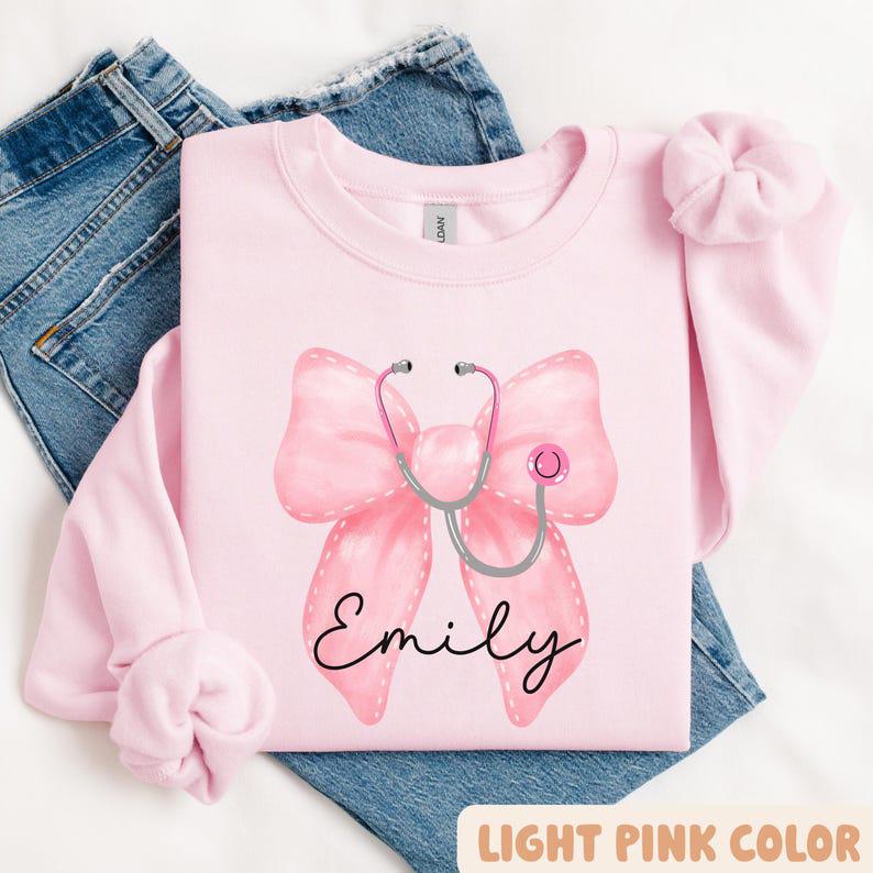 Custom Coquette Name Gift For Nurses, Healthcare Workers Sweatshirt, Pink Bow & Stethoscope Design, Nurse Bow Shirt, Christmas Nurse Gift, Unisex Shir